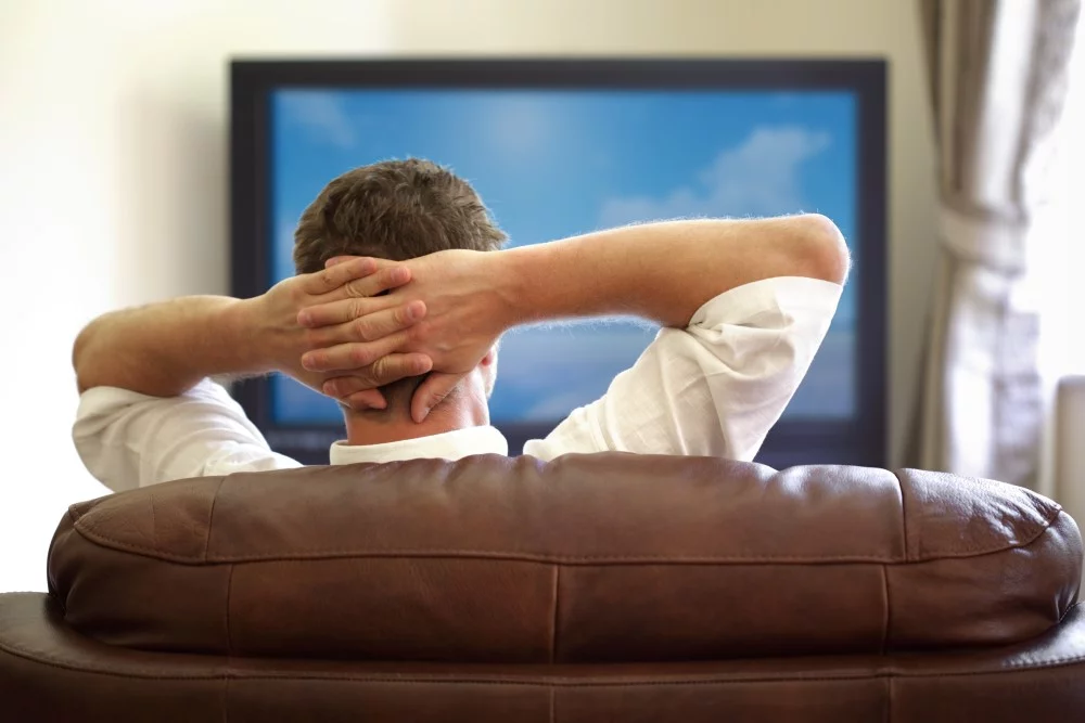 Mand der sidder i sofaen foran sit TV